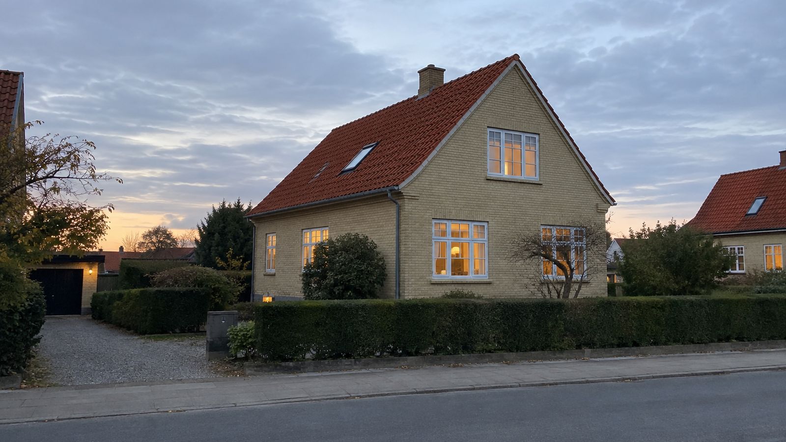 Dansk villa i skumring med varmt lys i vinduerne